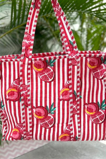 Red and white striped tote bag with fruit pattern on a green leafy background