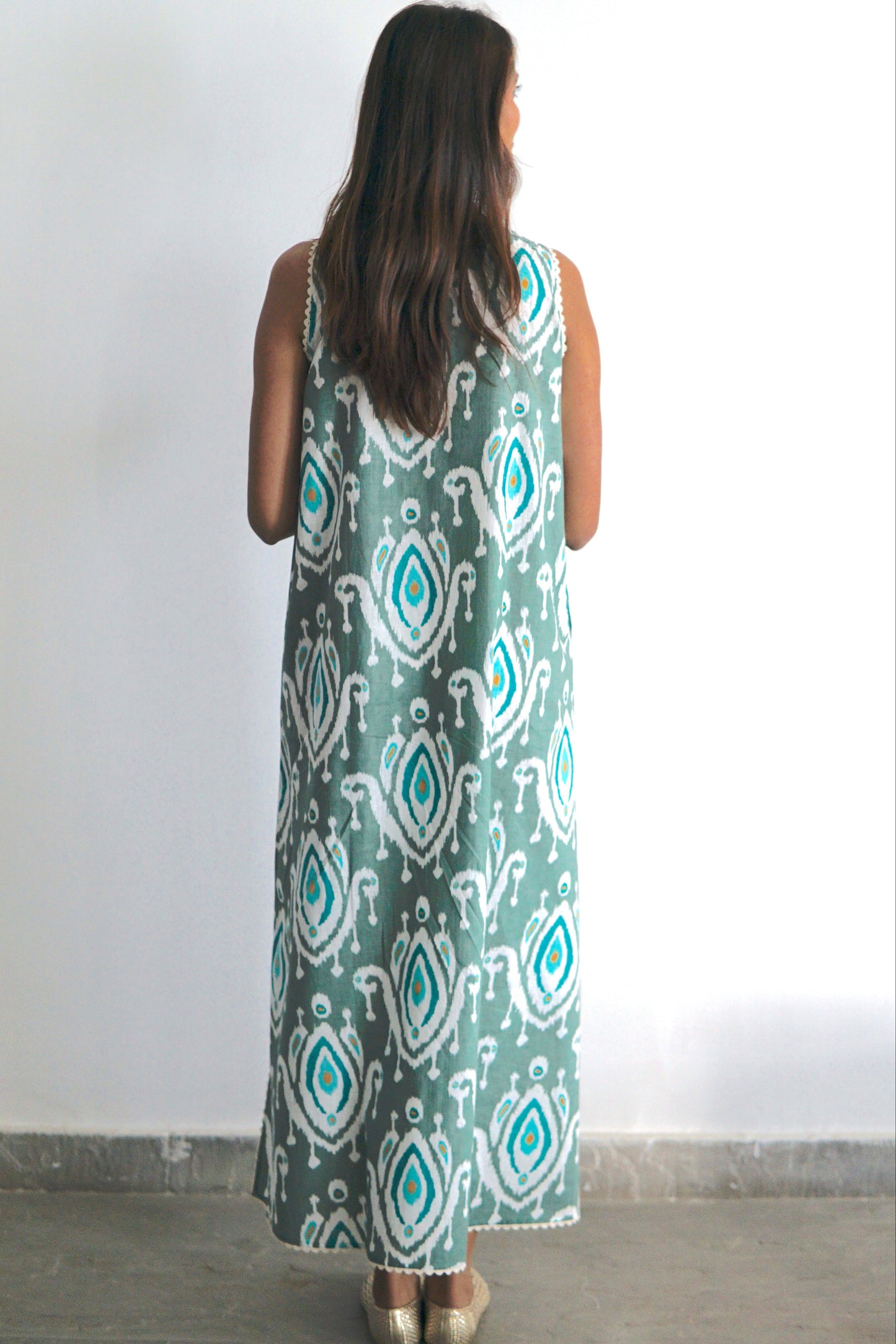 Woman wearing a long, patterned dress against a white wall.