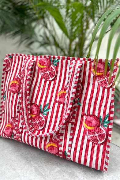 large Red and white striped tote with fruit pattern on a light surface with green plants in the background
