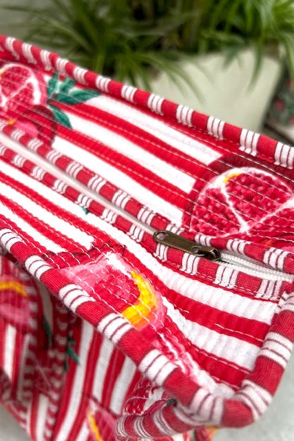 Red and white striped tite bag with fruit pattern on a light surface with green plants in the background