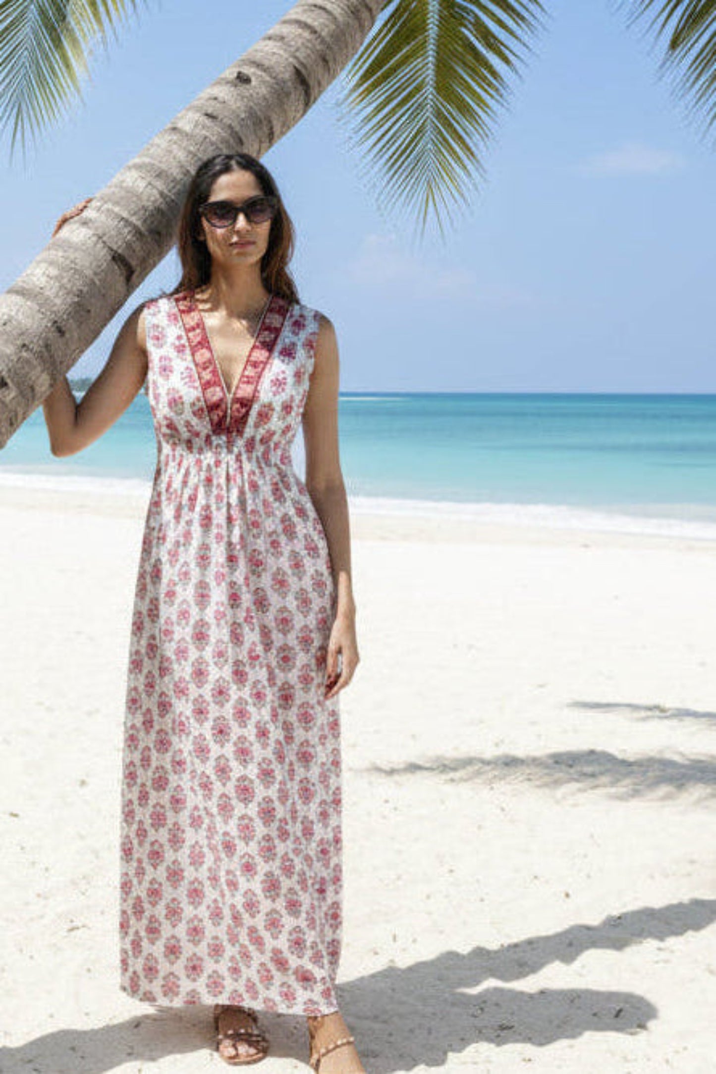 Woman in a floral dress standing under a palm tree on a tropical beach.