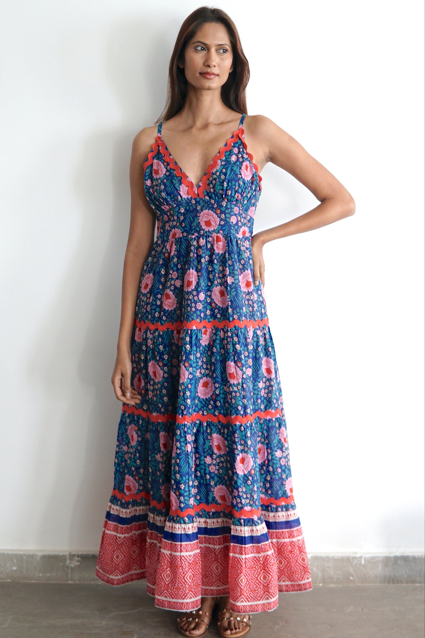 Woman wearing a blue and pink floral cotton maxi dress with ric rac trimming and pockets. 