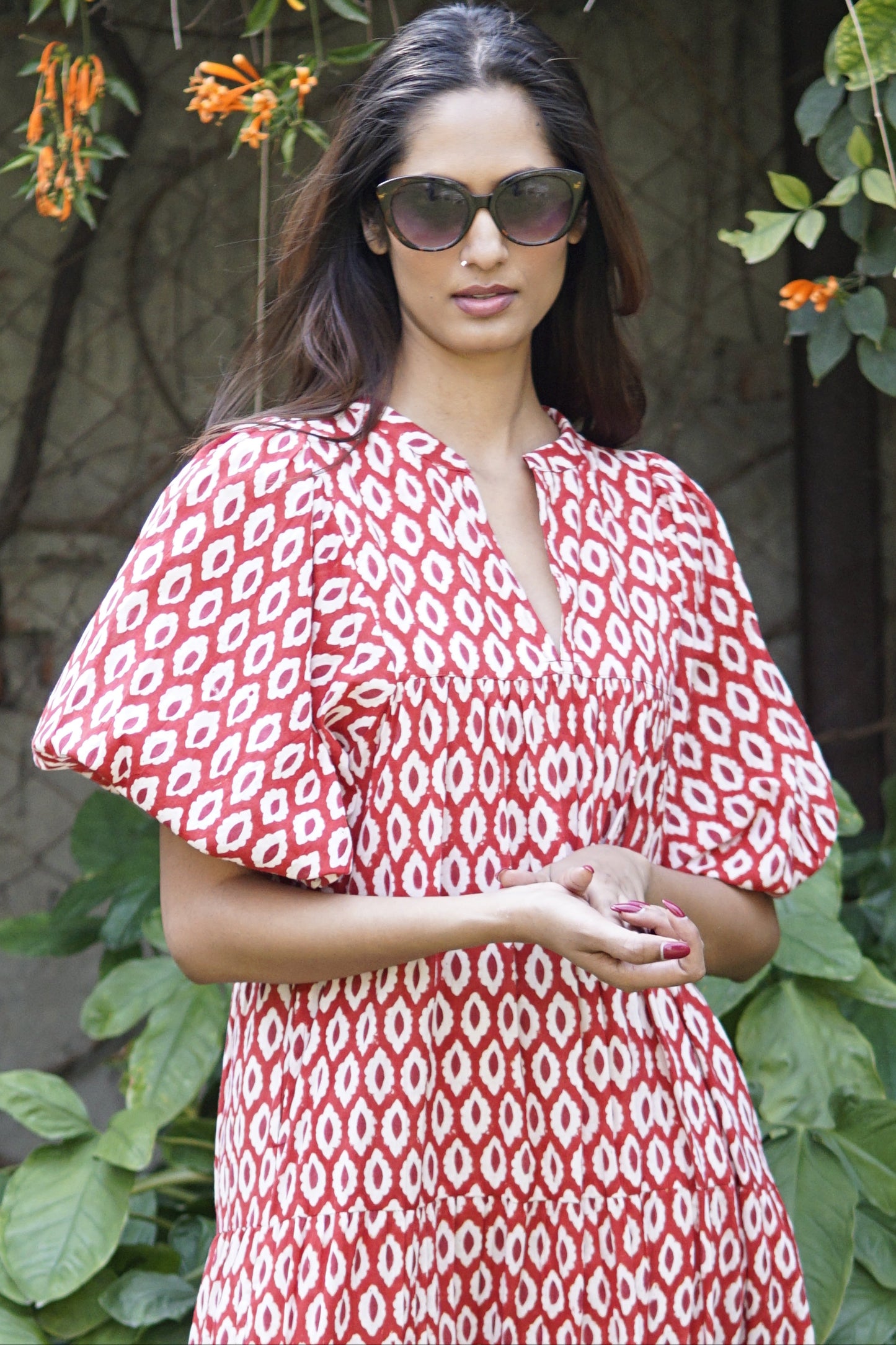 Woman wearing a red and white patterned dress with sunglasses outdoors.