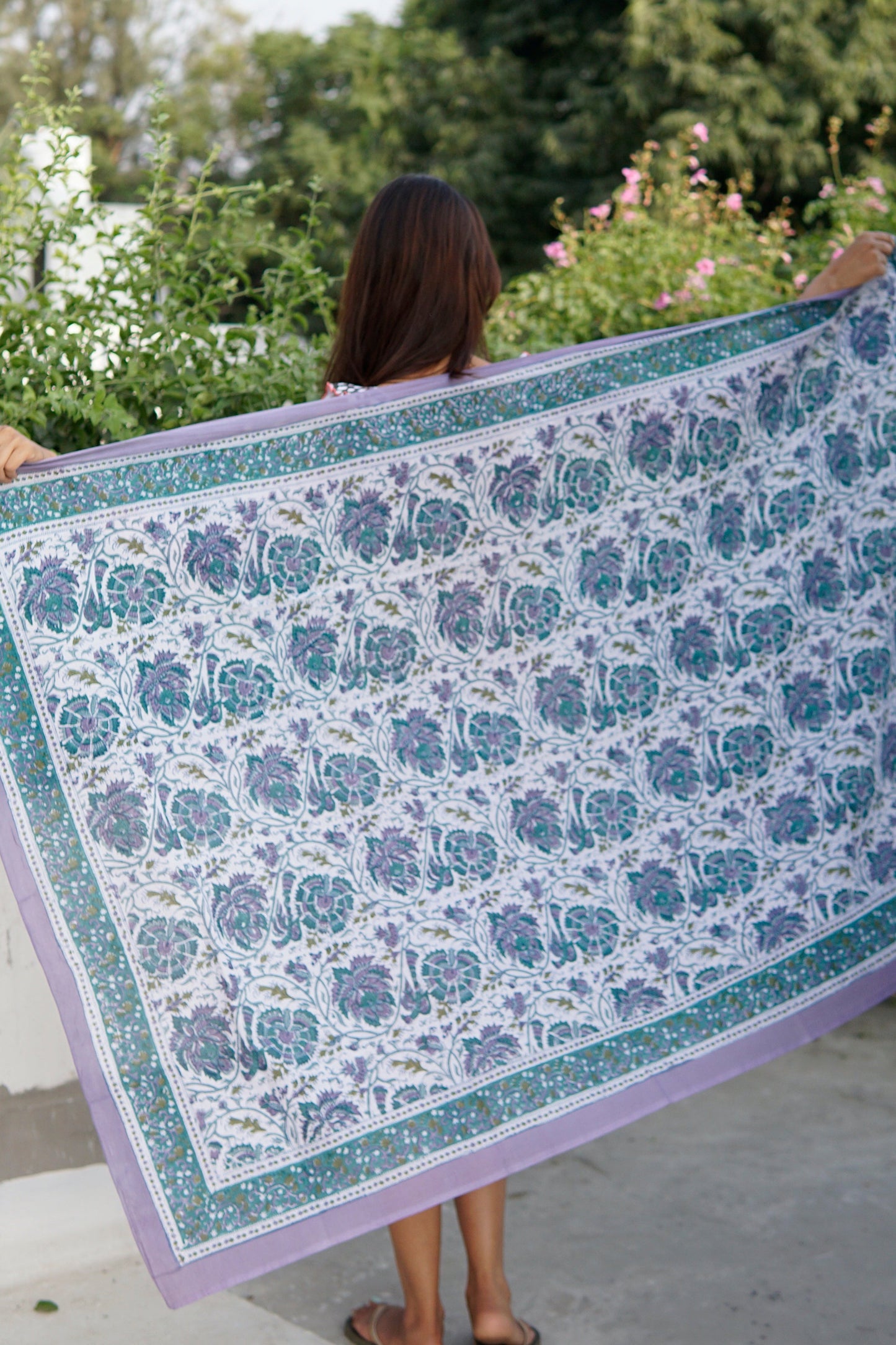 Person holding a large floral-patterned fabric outdoors with greenery in the background