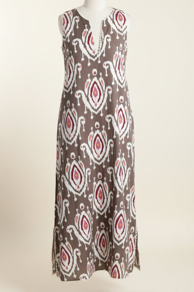 Woman wearing a sleeveless ikat print kaftan dress with a pattern against a white wall.